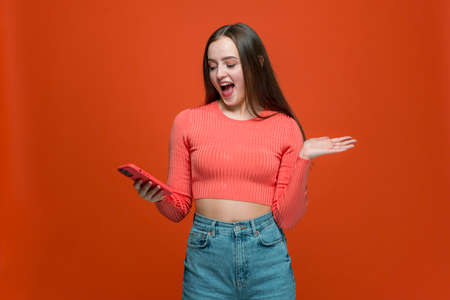 Amazed happy young girl using phone with surprised expression, reading shocking message on social network appsの写真素材