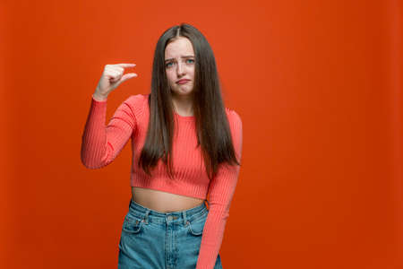 Dissapointed young girl showing small size or little bit gesture with fingers, low rating on orange backgroundの写真素材