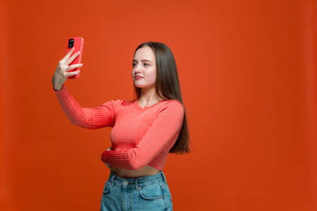 Pretty young girl looking at phone using mobile camera or apps taking selfie for social networks content, bloggingの写真素材