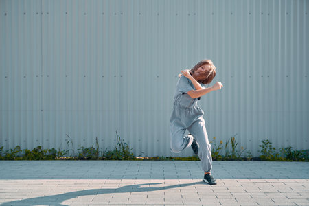 Dancing child girl happy moving on textured street fence background. Energetic cool teen female dancer having funの写真素材