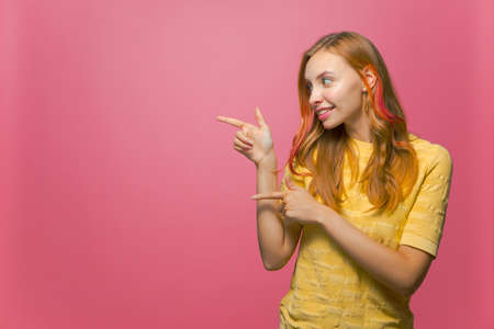 Beautiful smiling young girl pointing fingers aside at copy space on pink background. Promotion, advertisement mockupの写真素材