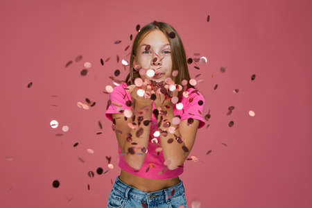 Happy little girl child celebrating holiday, blowing confetti glitters from palms to camera, Womens Day congratulationsの写真素材