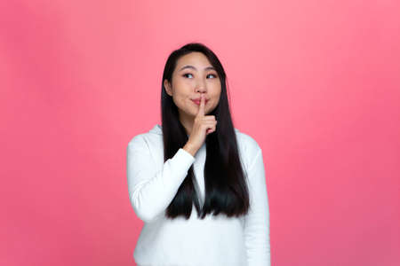 Silence gesture. Smiling young modern asian girl hold finger on lips ask to keep secret. Unique sale offer conceptの写真素材