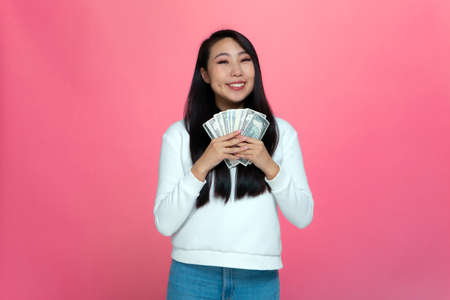 Happy rich young asian girl holding cash banknotes, enjoy money win, big financial profit and wealth on pink backgroundの写真素材