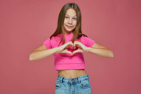Adorable little girl child showing love sign, making heart gesture on pink studio background. Charity, donation conceptの写真素材