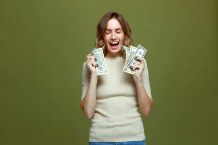 Joyful young woman with cash money in dollar banknotes, jackpot, laughing celebrating win on green...