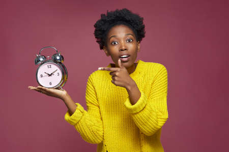 Hot deadline. Stressed worried young african american girl holding alarm clock pointing on remaining...