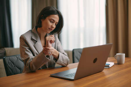 Tired young female businesswoman office worker holding wrist suffering pain in hand after long-term working on laptop.の写真素材