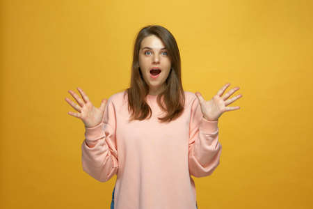 Amazed shocked young girl open mouth cant believe surprised by offer raising spread palms on yellow backgroundの写真素材