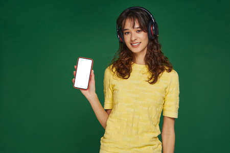 Modern young girl in headphones showing mockup blank screen phone with copy space for advertising....
