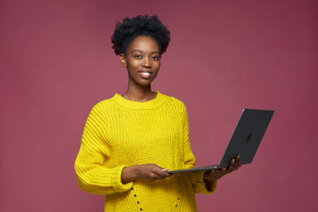 Smiling african american stylish young girl with modern laptop, satisfied with online shopping, remote job, web servicesの写真素材