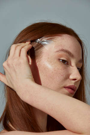 Redhead beautiful girl using fox eye lift tape for slightly upturned eyes shape. Beauty trend. Close-up studio portraitの写真素材
