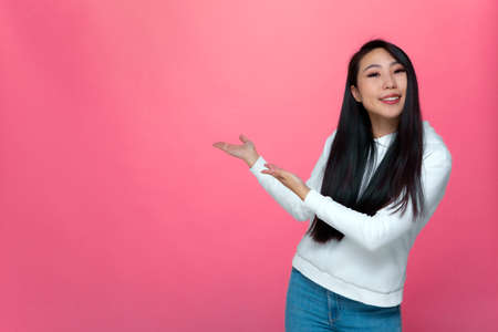 Smiling asian young girl showing new product, advertise services on pink background with copy space...
