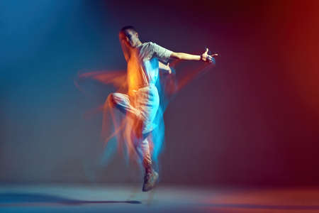Jumping young girl with short hair cool dancing in colorful neon light. Contemporary dance school ad. Long exposureの写真素材