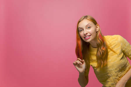 Friendly young girl smiling peek in shot with copy space on pink studio background with copy space...