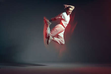 Energetic jumping young sporty girl in leap. Dance training. Breakdancer in red neon studio light....
