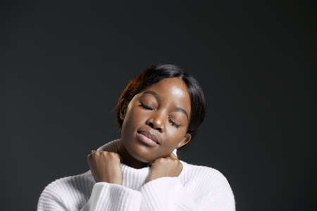 Calm pretty african american young woman with closed eyes holding collar of white winter sweater. No stress conceptの写真素材