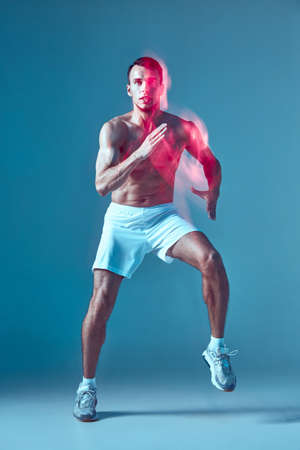 Dancing young guy with naked muscular torso performs zumba dance in neon light. Blurred motion....