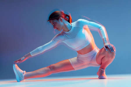 A girl in a white sports uniform is warming up. A fitness model on a blue background performs exercises with long exposure effect.の写真素材