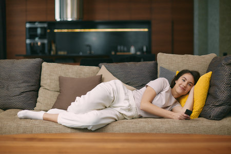 Relaxed young girl watching television, series or movie, lying on sofa in cozy modern living room, rests at homeの写真素材
