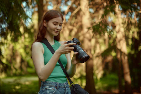Young woman in green top enjoys taking pictures in the forest. Pretty girl is holding camera in her hands.の写真素材