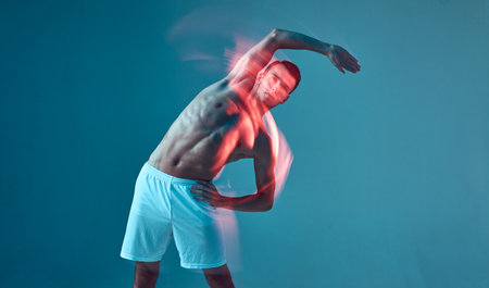 Athletic young male with naked muscular torso exercise, makes side tilts, raised arm. Long exposure, motion blurの写真素材