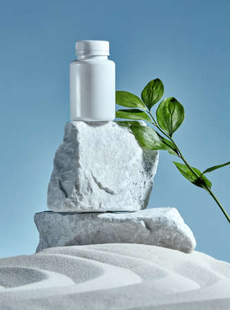 Stone podium on a blue background with big leaf and white sand. Nature, sand, leaf, stone. Storage for beauty products.の写真素材