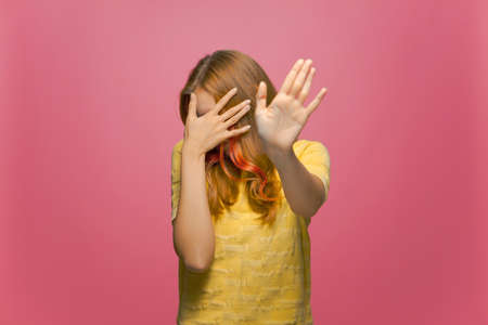 Scared or embarrassed young girl covering eyes with hands and doing stop gesture on pink studio backgroundの写真素材