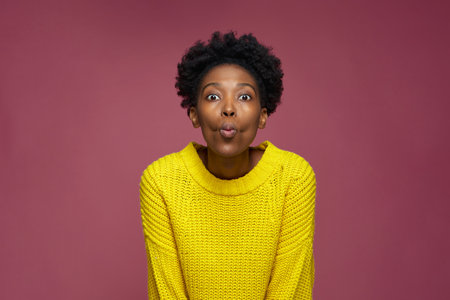 Funny african american girl makes faces with big eyes and pouting lips, looking at camera. Silence,...