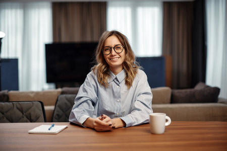 Smiling female employee wearing glasses sitting at office desk looking at camera. Job interview, hr, employment conceptの写真素材