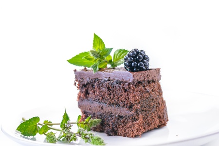 Detail of home made chocolate cake with blackberry and mint on white background.