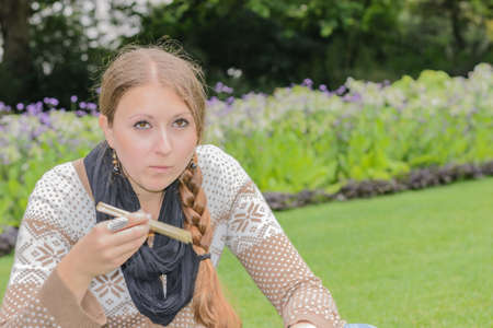 Woman eating sushi and smiling in the park with flowers の写真素材