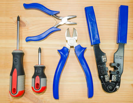 A tongs, pliers, Crimping pliers and two screwdrivers on a wooden board