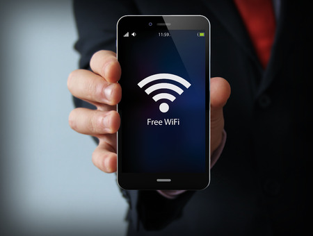 business and mobility communications concept: businessman holding a modern smartphone with free wifi zone icon