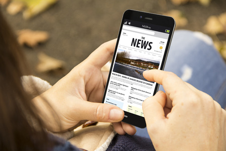 media technology and modern lifestyle concept: young woman with smartphone reading the news at the parkの写真素材