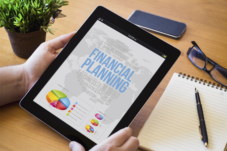 hands of a man holding a financial planning device over a wooden workspace table. All screen graphics are made up.