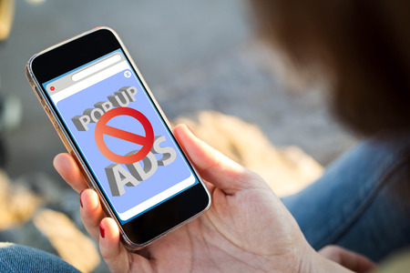 close-up view of young woman checking her mobile phone with ads blocked on the screen. All screen graphics are made up.の写真素材