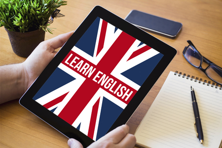 hands of a man holding a learn english device over a wooden workspace table. All screen graphics are made up.