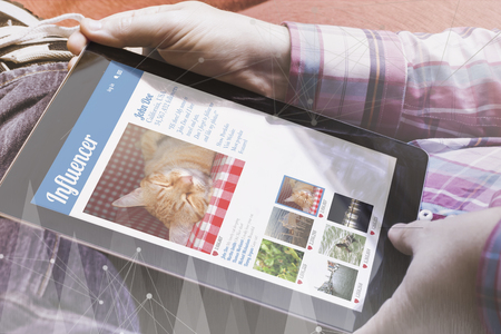 close-up view of man holding a tablet showing influencer social media profile. All screen graphics...