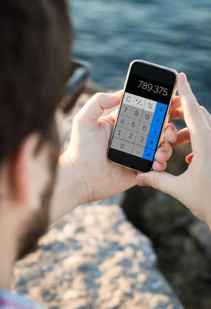 Man with sunglasses using a calculator app on smartphone near the sea