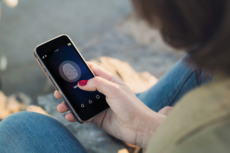 woman holding a smartphone and touching the screen to unlock it. All screen graphics are made up.の写真素材