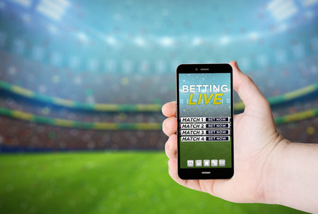 Hand hold a phone with  betting online on a screen on the background of a stadium.の写真素材