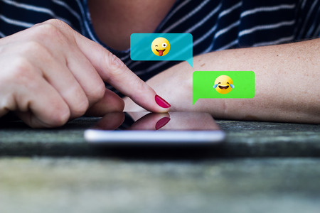 Close-up of a hands of a woman using emojis to chat. All screen graphics are made up.