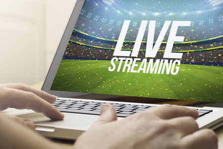 live streaming concept: man using a laptop with sports event on the screen. Screen graphics are made up.の写真素材