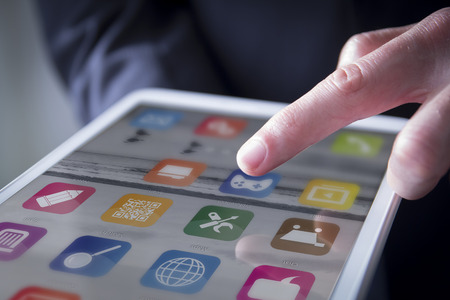 finger touches digital tablet showing apps on screenの写真素材