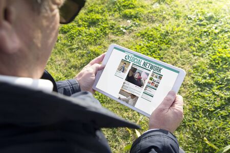 Old man holding digital tablet pc with social network app. All screen graphics are made up.