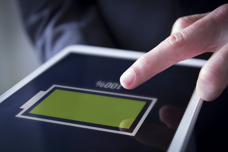 finger touches digital tablet showing full battery on screen