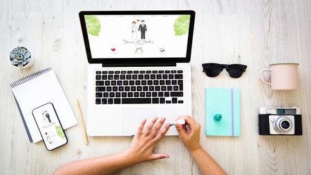 Female hands doing nail polish and browsing a wedding website invitation. All graphics are made up.の写真素材