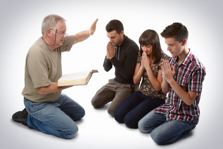 Preacher leading three young souls in prayer to receive Jesusの写真素材