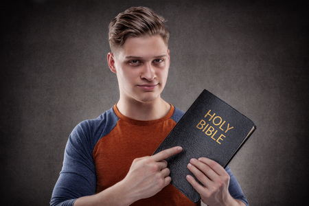 Happy young man pointing his Holy Bible with leather coversの写真素材